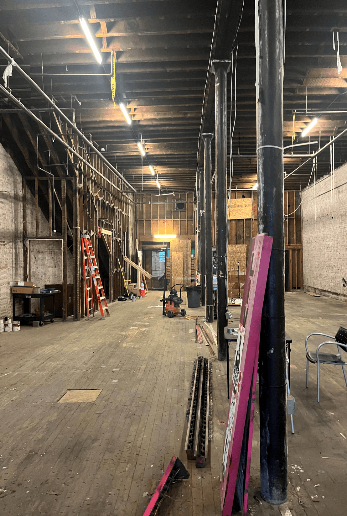 Inside the Seven Seas Building today: the gutted main floor mid-restoration, original timber columns and 1890 brick exposed, work lights on