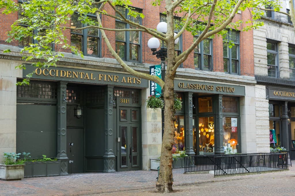 The Occidental Fine Arts Center storefront in summer daylight on a tree-lined Pioneer Square block in Seattle.