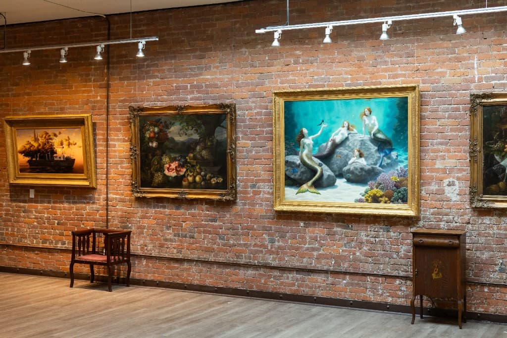 Brick-walled main gallery at the Occidental Fine Arts Center with gilt-framed paintings hung salon style.